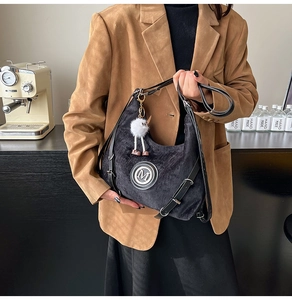 Détail d'un sac d'épaule en velours noir avec logo M et breloque pompon en peluche
