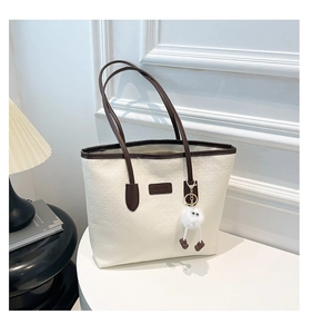 Close-up of cream tote bag with embossed pattern, brown straps and plush monster charm