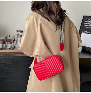 Détail du sac bandoulière rouge matelassé avec large sangle à motifs stylisés