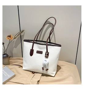 Detail view of white embossed tote bag with brown leather straps and plush monster charm