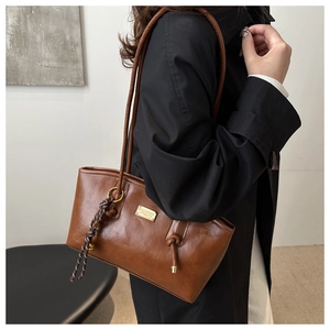 Detail of caramel brown retro tote bag featuring gold hardware and a woven knot charm