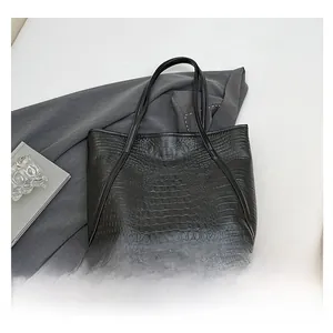 Détail d'un sac cabas noir à motif crocodile posé sur une tenue de bureau grise