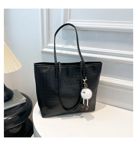 Detail of black faux leather tote with embossed texture and cute plush monster charm