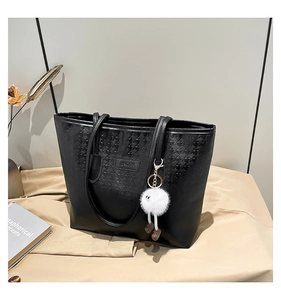 Detail of black tote bag with houndstooth embossing and plush cartoon pendant accessory