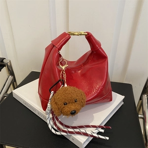 Chic red faux leather handbag with teddy charm and gold clasp on a book background