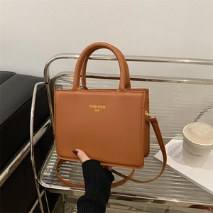 Brown PU leather square handbag with dual handles and adjustable strap on a metal shelf