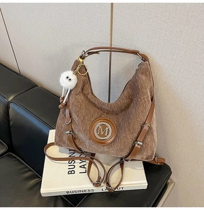 Détail du sac en velours côtelé marron avec logo M argenté et breloque pompon blanc
