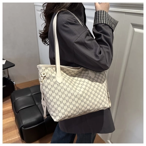 Detailed view of the monogram printed tote bag worn by a model in a modern indoor setting