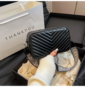 Sac bandoulière matelassé noir avec bandoulière large à motifs et emballage cadeau chic