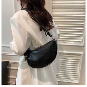 Minimalist black crescent shoulder bag with knot detail shown in a stylish studio setting