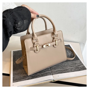 Detail of light beige tote bag with round handles, metal twist lock, and crossbody strap