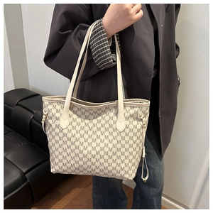 Detailed shot of woman wearing a cream tote bag with M-pattern print on shoulder