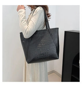 Vue latérale d'un grand sac cabas noir à texture crocodile porté par un mannequin chic