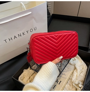 Détail d'un sac rouge en similicuir matelassé avec une large bandoulière tissée ethnique