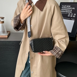 Sac bandoulière matelassé noir avec large sangle géométrique porté sur un trench beige