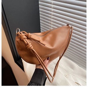 Detail of a brown vegan leather crescent bag featuring a knotted strap and silver metal rings