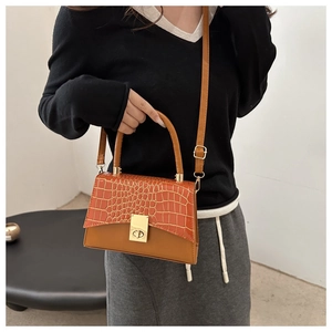Sac à main marron avec rabat texture crocodile et boucle dorée porté par un mannequin