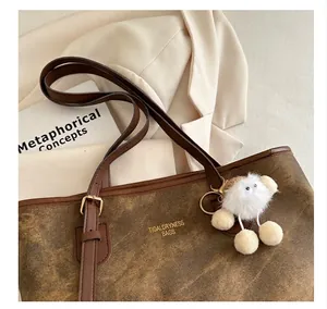 Detailed macro view of a brown tote bag with gold logo and fluffy white doll pendant