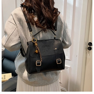 Detail view of black vintage leather backpack with buckle straps and bell charm accessory