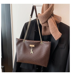 Detail of dark brown woven shoulder bag with gold deer charm on black blazer