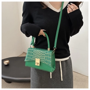Détail d'un sac bandoulière vert effet croco avec fermoir doré porté par un mannequin
