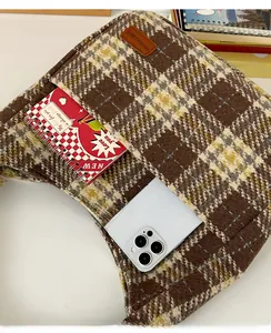 Detail of front pocket on brown checkered tote bag holding a phone and notebook