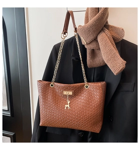 Close-up of woven brown tote bag featuring a golden deer charm and chain strap