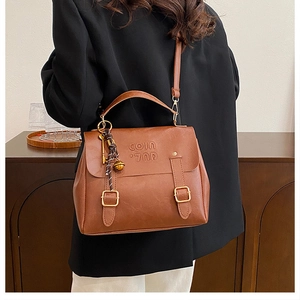 Detail of dark brown matte PU leather handbag with embossed letters and metal charm
