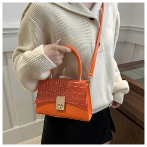 Détail d'un sac à main orange vif avec texture crocodile, fermoir doré et fine bandoulière