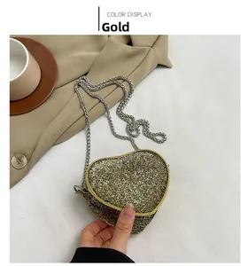 Detail of a heart-shaped mini gold sequin bag with silver chain strap shown by hand