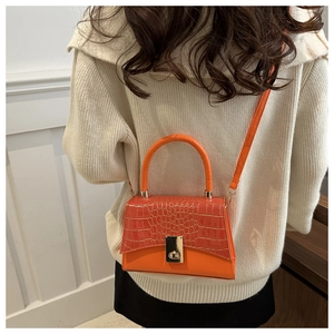 Détail du sac à bandoulière orange vif avec texture crocodile et fermoir doré sur un modèle