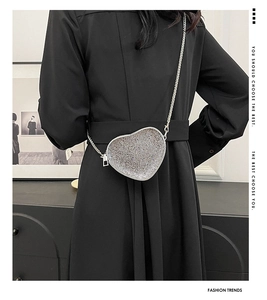 Detail of heart-shaped rhinestone evening bag with silver crystals and chain strap worn by model