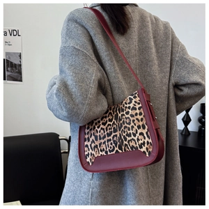 Detail view of leopard print shoulder bag with burgundy leather trim worn by model