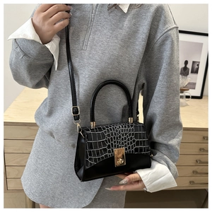 Détail du sac noir avec motif crocodile et fermoir rotatif en métal doré élégant