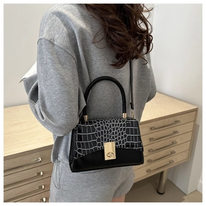 Détail d'un sac à main chic en cuir noir texturé avec un fermoir doré sur un socle en bois