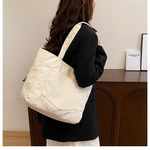 Detail view of white corduroy tote bag featuring an outer pocket and soft ribbed texture