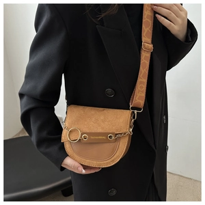 Détail du sac selle en daim marron avec anneau doré et large bandoulière géométrique