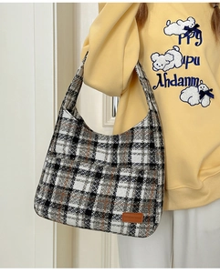 Close-up of checkered hobo bag with leather logo tag on model in yellow hoodie