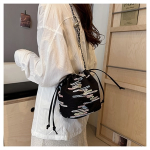Close-up of black drawstring bucket bag with colorful wavy embroidery and chain strap