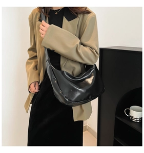 Dettaglio di una borsa hobo nera lucida indossata da una modella in stile minimalista
