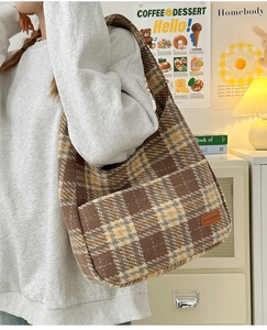 Detail view of plaid tote bag featuring textured tweed fabric and leather brand patch