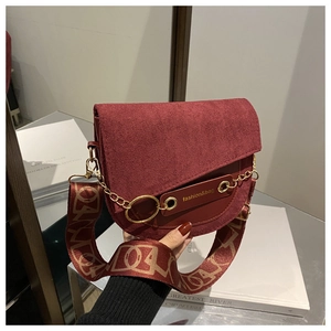 Détail du sac selle bordeaux montrant la texture mate et la boucle dorée avec chaîne