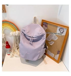 Detailed close-up of light purple nylon backpack with B.a.g embroidery and cord zippers