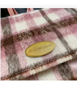 Détail du tissu en laine à carreaux roses et plaque logo en métal doré sur un sac à dos