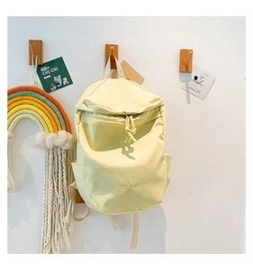 Detail of light yellow nylon backpack with front zipper pocket and embroidered Bag logo