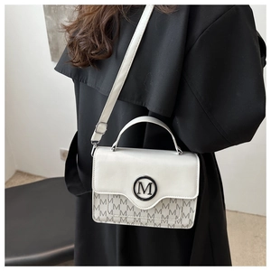 Detail van witte crossbodytas met M-print en ronde metalen gesp op de voorkant