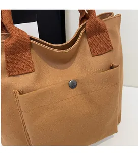 Détail du sac cabas en toile marron montrant le tissu texturé, la poche et le bouton pression