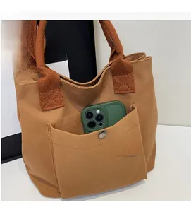Détail d'un sac cabas en toile marron avec une poche extérieure et boucle métallique de sécurité
