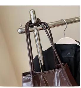 Detail view of deep chocolate leather tote bag handles hanging on a metal hanger
