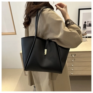 Dettaglio borsa tote nera con fibbia dorata su modella con trench e stile minimalista